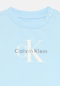 T-shirt en coton bleu clair avec un col rond, présentant un logo imprimé "Calvin Klein" en blanc et gris sur la poitrine.
