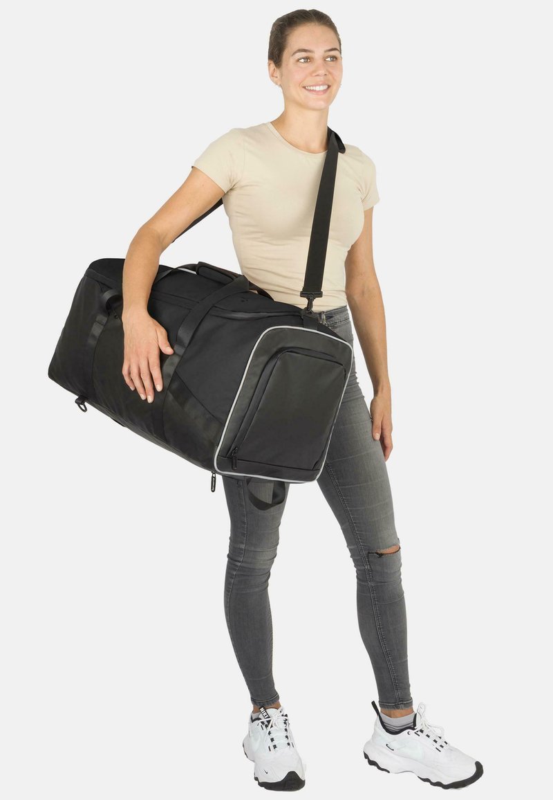 Schwarze Sporttasche mit strukturiertem Design, ausgestattet mit weißen Akzenten, Reißverschlusstaschen und verstellbarem Schultergurt. Wird über einer Schulter getragen.