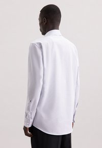 Camicia bianca a maniche lunghe con un sottile motivo a quadri, orlo dritto e bottoni ai polsini. Tessuto morbido con un design di colletto classico.