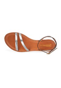 Sandal de cuero marrón con dos tiras metálicas plateadas y un cordón de tobillo marrón. Presenta detalles cosidos y una plantilla con marca.