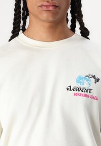 Hvit bomulls t-skjorte med rund hals. Har et blått måne grafikk og svart tekst "ELEMENT" og "NATURE CALL" i rosa. Myk tekstur.