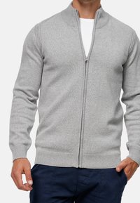 Grå lynlås-trøje med høj krave, ribstrikkede manchetter og kant, lavet af et blødt, strikket stof med en glat tekstur.