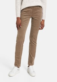 Pantalons en velours côtelé marron à coupe slim, présentant des côtes verticales discrètes et des poches standard, associés à des baskets blanches.