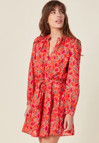 Punainen kukallinen mekko pitkähihaisilla, kauluksen omaavalla pääntiellä ja vyötärösoljella. Sisältää kerrokselliset hameet, joissa on eläväinen tulppaanikuvio.