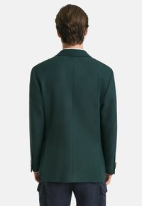 Blazer ajusté vert foncé, en tissu mélangé laine, fente simple au dos, revers crantés, forme ajustée, accents de manche à trois boutons.