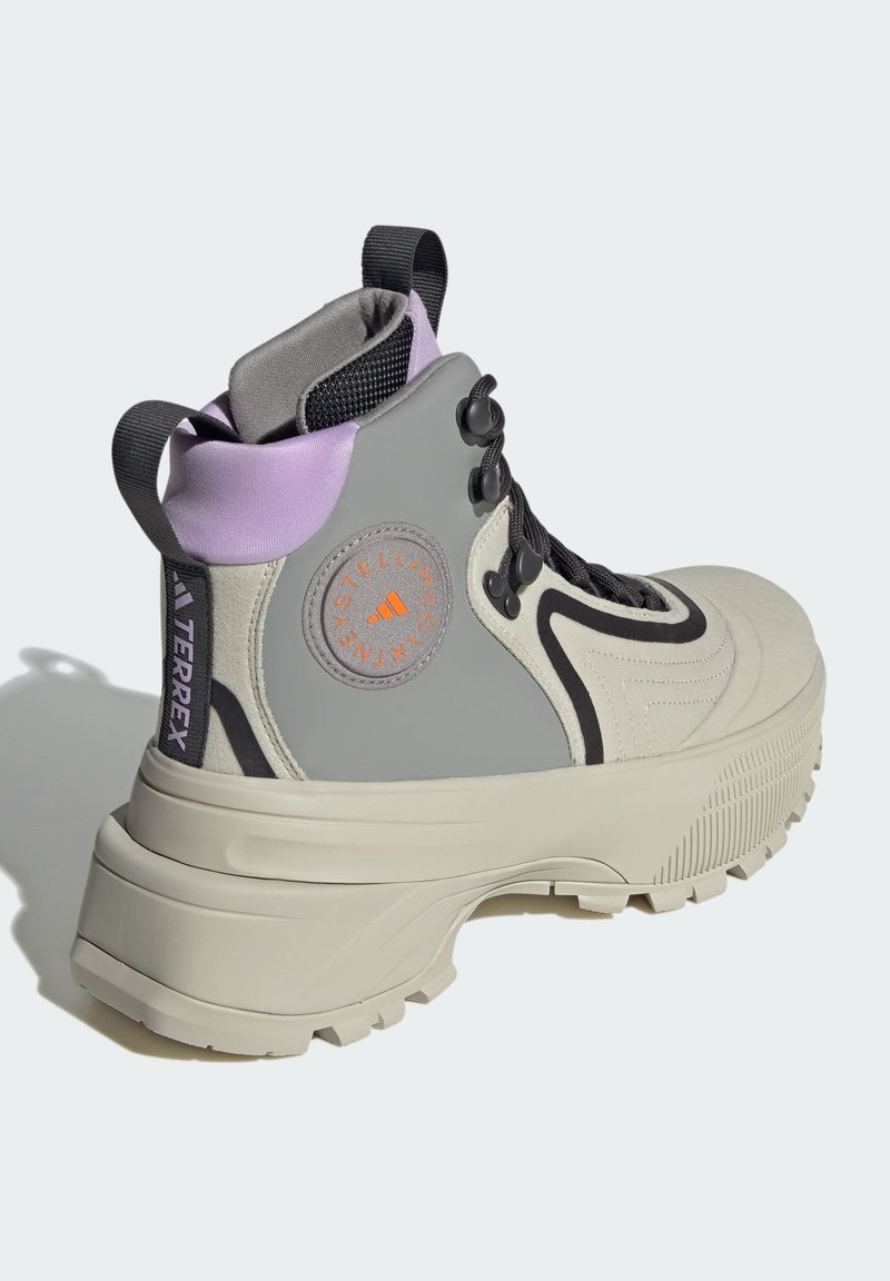 Szare buty trekkingowe z grubą beżową podeszwą, fioletowym kołnierzem i czarnymi sznurowadłami. Posiadają logo po boku oraz okrągłą naszywkę z pomarańczowymi detalami.