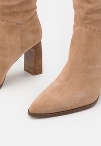Bottines en daim camel à bout pointu et talon bloc en bois. Le matériau possède une texture douce avec une finition lisse.