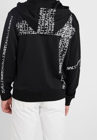 Czarna bluza z kapturem z białym nadrukiem, z graficznym wzorem na plecach i rękawach. Wykonana z miękkiego, teksturowanego materiału.
