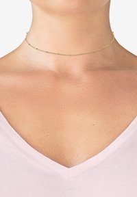 Gold choker necklace featuring a delicate chain with small spherical accents, worn on a bare neck, against a light pink garment.