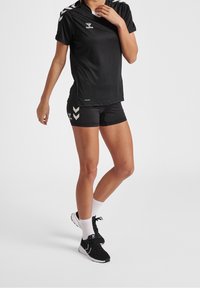 Svart idrottströja och shorts med vita accenter, med en logotyp på bröstet och chevron-mönster på shortsen. Lämplig för sport.