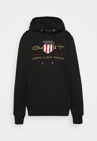 Sudadera negra hecha de una mezcla de algodón. Cuenta con un bolsillo frontal tipo canguro, puños de canalé y un logo dorado bordado con un diseño de escudo y texto.