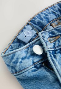 Tissu en denim bleu clair avec une texture légèrement délavée. Présente un bouton bleu et des accents de boutons métalliques argentés avec des coutures contrastées.