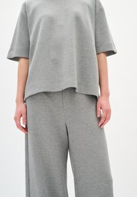 Completo in cotone grigio, composto da una maglietta a maniche corte ampia e pantaloni a gamba larga, entrambi con una texture morbida e dettagli di cucitura minimal.