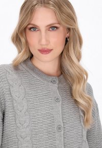 Cardigan lavorato a maglia grigio chiaro con un motivo a coste testurizzato, un design a trecce su un lato e bottoni rotondi sulla parte anteriore.