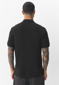 Mustast polo-särgist klassikalise disainiga. Lühikeste varrukatega, pehmest kangast ja kraega. Omab sirget lõiget ilma nähtavate mustriteta.