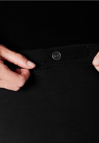 Svart tygmidjeband med knappstängning framtill, visar en hand som justerar passformen. Slät textur och elastiskt material.