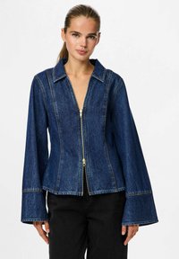 Denim jakna z zadrgo spredaj, velikimi kragi in razširjenimi rokavi. Temno modra tkanina s kontrastnim rumenim šivanjem.