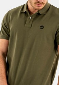 Polo shirt verde oliva realizzato in tessuto testurizzato, con colletto, patta con due bottoni e un piccolo logo nero sul petto.