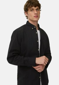 Schwarzes Button-Down-Hemd mit einem Kragen, ausgestattet mit einer Brusttasche, hellen Knöpfen und einem leichten Stoff, gestylt mit aufgekrempelten Ärmeln.