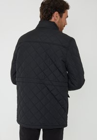 Zwarte gewatteerde jas met een staande kraag, voorzien van een diamantpatroon, middellange snit en zijzakken.