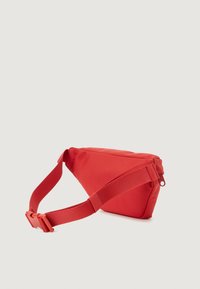 Red triangular crossbody bag made of durable fabric with a single adjustable strap and a zip closure at the top. Features minimalistic design.