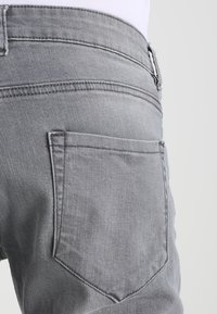 Jeans de mezclilla gris con una vista en primer plano del bolsillo trasero. Las características incluyen un corte recto y detalles de costura sutiles.