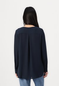 Mørkeblå langermet bluse i glatt stoff, med rund hals, plissé detaljer bak og knappede mansjetter. Kombinert med lyse denim.