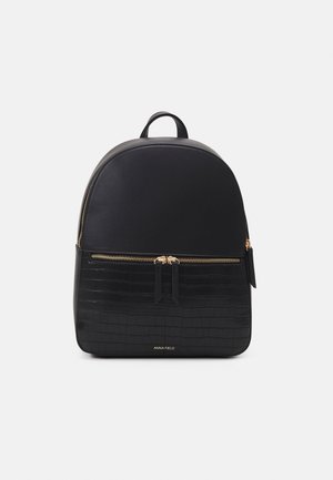 Zaino nero con una parte superiore in tessuto liscio e una texture in pelle di coccodrillo nella sezione inferiore; dotato di hardware dorato e chiusura con doppia zip.