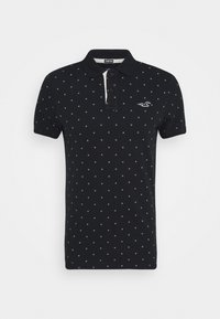 Svart polo-shirt i stretchmaterial. Har små vita rutmönster, en kontrasterande vit krage och en logga på bröstet.