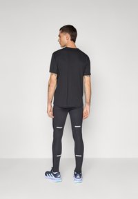 Chemise noire à manches courtes et leggings noirs avec des accents réfléchissants, associés à des chaussures de sport foncées. Tissu lisse, silhouette ajustée.