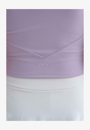 Levandulový top s krátkým rukávem vyrobený z hladkého materiálu s V-výstřihem a jemným brandingem na lemu. Doplňený bílou sukní.