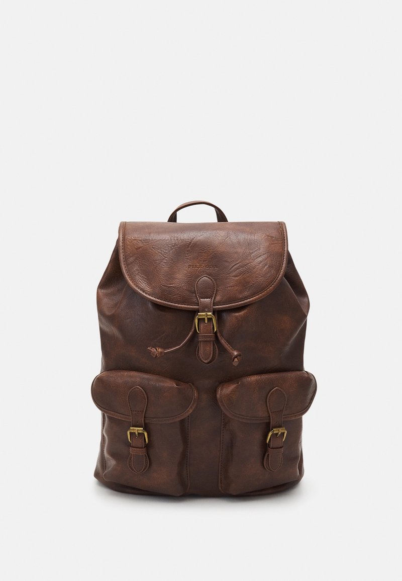 Sac à dos en cuir marron avec rabat supérieur et fermeture à boucle, deux poches avant à boucle et une petite poignée de transport sur le dessus, présenté sur fond blanc.