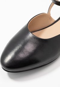 Czarne skórzane buty z okrągłym noskiem i wyciętymi bokami. Gładka tekstura, minimalistyczny design i pasek na kostkę dla pewnego trzymania.