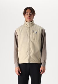 Beige fleece vest with high collar, zippered chest pocket, and gray long sleeves. Soft texture and casual design, no visible patterns.