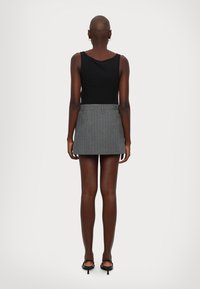 Un débardeur noir associé à une mini-jupe grise à rayures. La jupe a une taille ajustée et des passants de ceinture visibles. Des sandales à talons hauts et fines complètent le look.