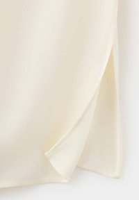 Gros plan d'un tissu crème avec un coin plié montrant une texture lisse et des bords cousus propres.