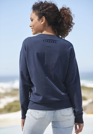 Navy blue sweatshirt with a relaxed fit, ribbed cuffs, and hem; features subtle logo "ELBSAND" on the back. Paired with light blue jeans.