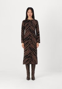 Abito a maglia a strisce zebra marroni e nere con maniche lunghe e taglio dritto, abbinato a stivali marroni al ginocchio.