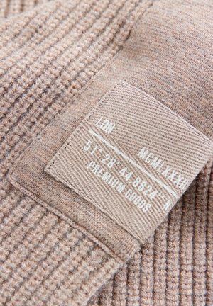 Tessuto di colore marrone chiaro con trama a coste, con un'etichetta in tessuto cucita che riporta le istruzioni per la cura e i dettagli della taglia.