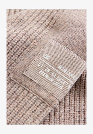 Světle hnědá texturovaná látka s žebrovaným vzorem, s přišitým štítkem z látky obsahujícím pokyny pro péči a informace o velikosti.