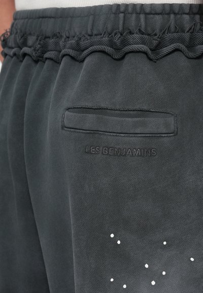 Tmavošedé tepláky s texturovaným pásom so strapcami, zadnou vreckom a bielymi bodkami blízko spodnej časti.