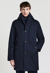 Cappotto lungo blu navy con cappuccio, dotato di chiusura con zip, quattro bottoni, taschino sul petto e tasche laterali, realizzato in tessuto liscio.