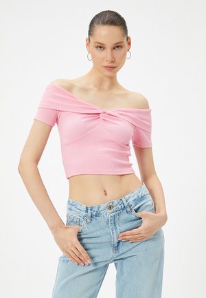 Top corto off-the-shoulder de canalé en color rosa con un diseño de frente torcido, combinado con vaqueros de mezclilla de tiro alto en azul claro. Textura suave, estilo ajustado.