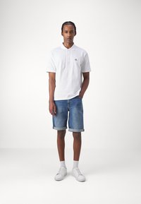 Vit pikétröja med korta ärmar och en texturerad tyg, kombinerad med uppkavlade denimshorts. Vita sneakers fulländar outfiten.