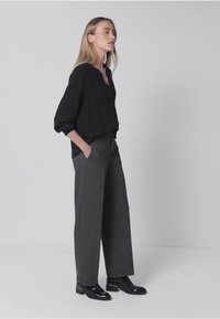 Svart blus med lösa ärmar och knäppt halsringning, matchad med högmidjade grå vida byxor och polerade svarta ankelstövlar.