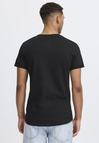 Camiseta negra de manga corta con cuello redondo, hecha de algodón. Textura suave y ajuste casual, vista desde la parte de atrás sobre un fondo sencillo.
