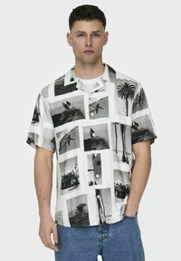 Camicetta a maniche corte in tessuto leggero con stampe fotografiche in bianco e nero di surfisti e palme su sfondo bianco.
