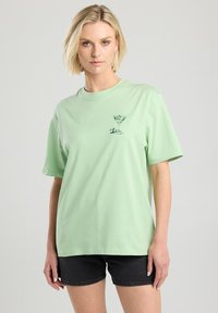 Mint green cotton t-shirt with short sleeves and a round neckline, featuring a black martini glass graphic on the front.