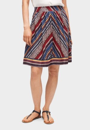 Jupe multicolore avec des motifs diagonaux rouges, bleus et blancs. Présente des plis, une forme évasée et un ourlet avec une garniture décorative.