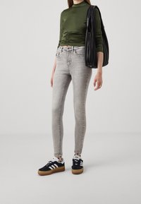 Vaqueros skinny de mezclilla gris combinados con una camiseta de manga larga verde oscuro. Zapatillas negras con detalles blancos. Bolsa tote negra con textura plisada.